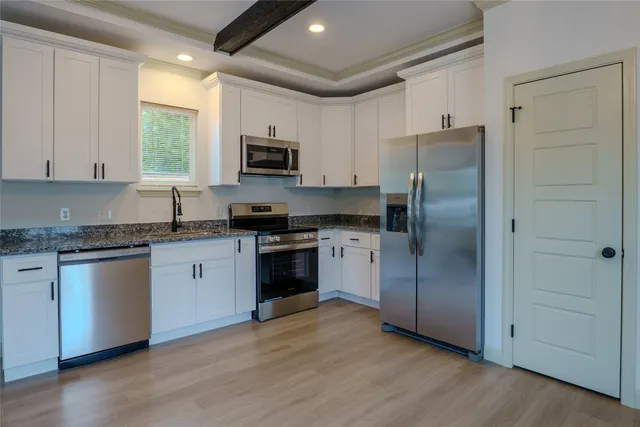 a kitchen with granite countertop a refrigerator a sink dishwasher a stove and a microwave oven with wooden floor