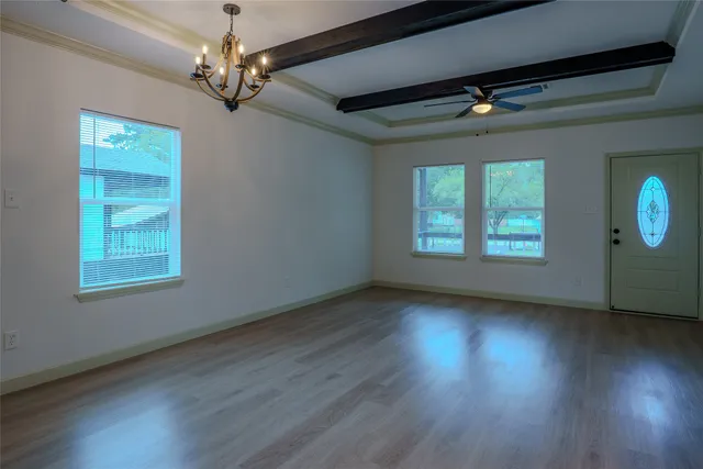 an empty room with wooden floor chandelier and windows