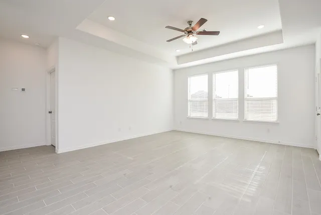 an empty room with chandelier fan and windows