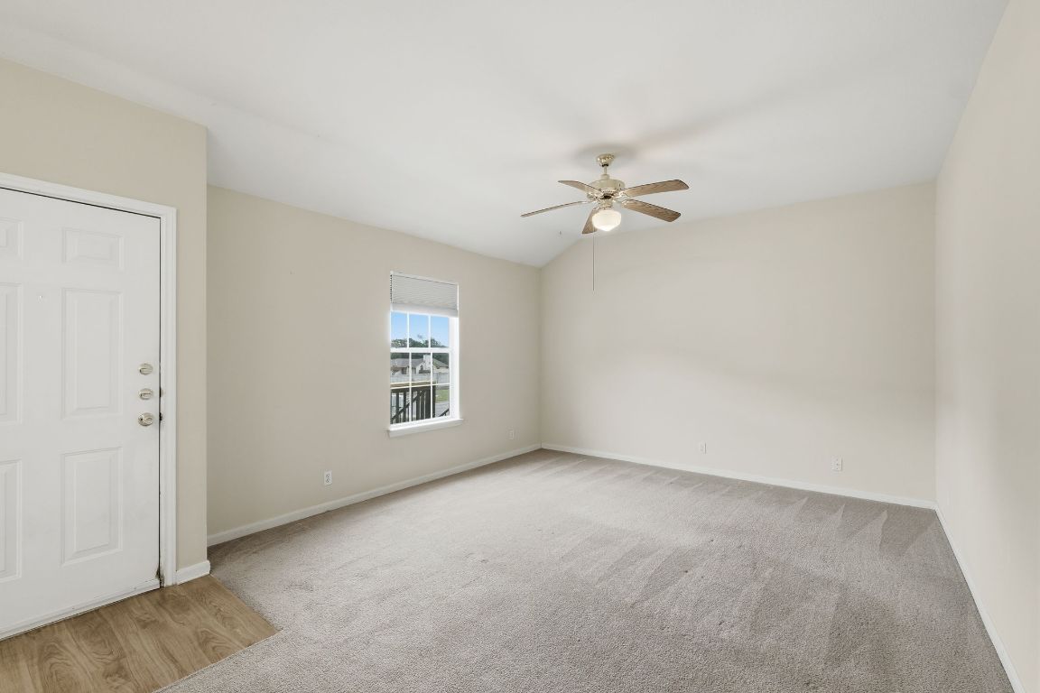 Unfurnished room featuring light colored carpet, vaulted ceiling, ceiling fan, and light wood-type flooring