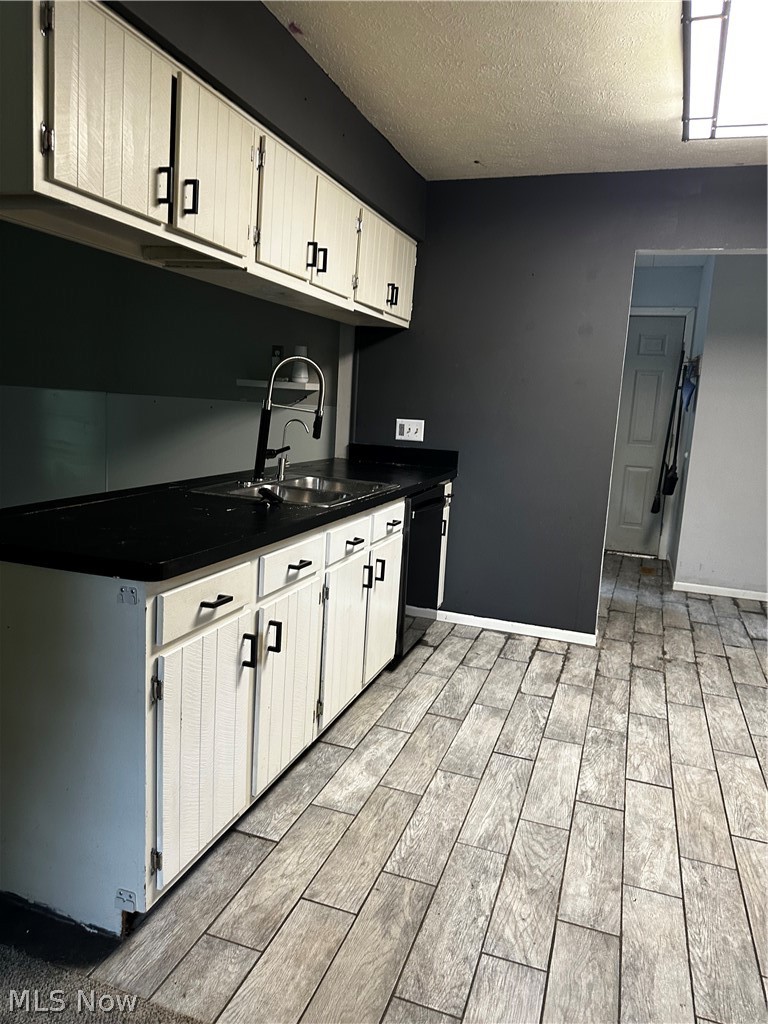 198 Park Road Painesville, OH 44077 - Photo 9 of 31 Kitchen featuring wood-finish plank flooring, white cabinetry with black hardware, dark countertops, and a dual basin sink with a high-arch faucet