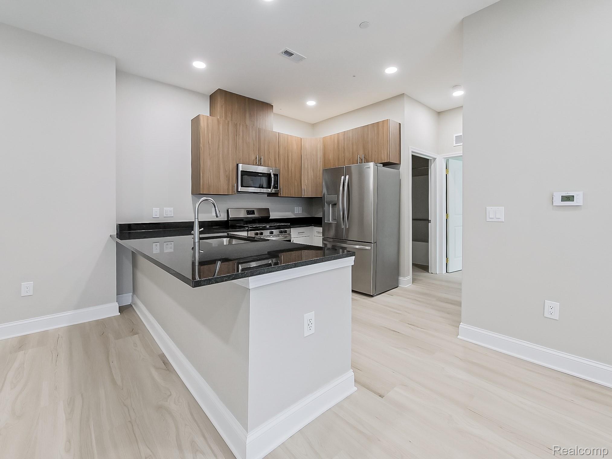31480 Warren Road, Unit 101 Westland, MI 48185 - Photo 3 of 26 Kitchen featuring dark stone countertops, stainless steel appliances, brown cabinetry, light wood-style floors, and a peninsula