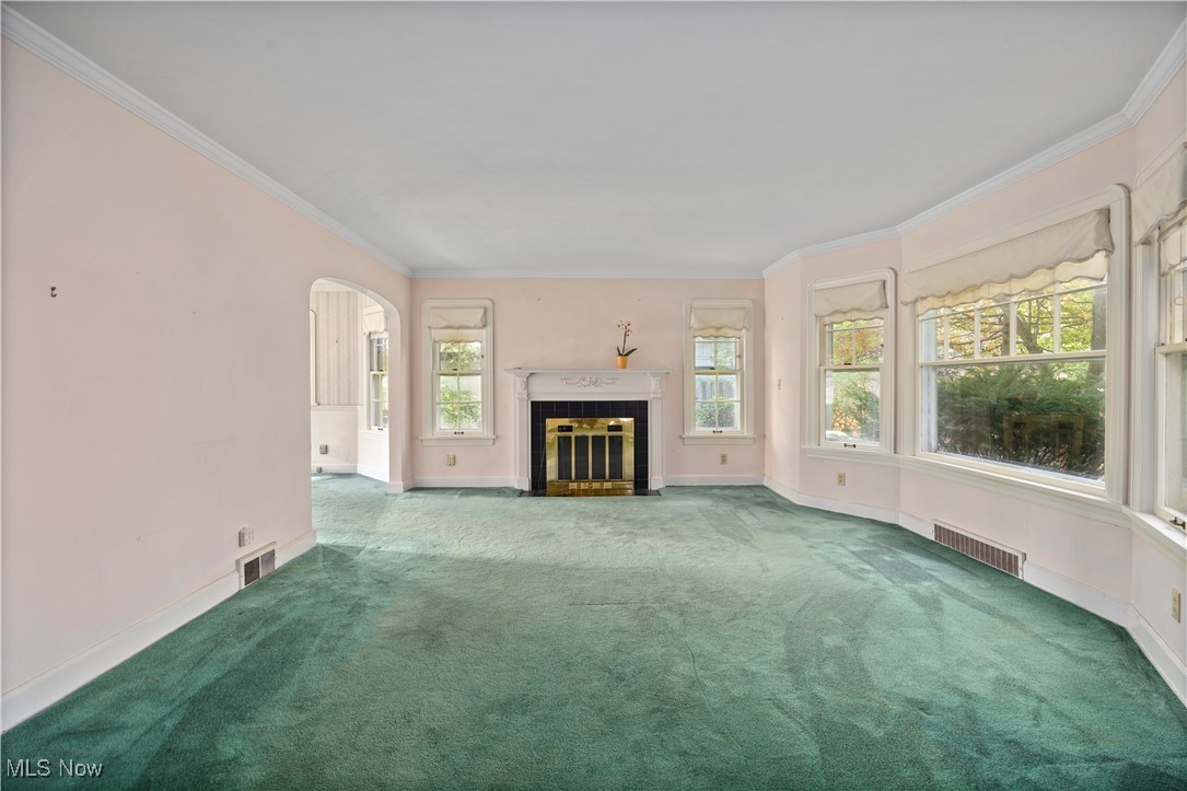 Unfurnished living room with arched walkways, ornamental molding, carpet flooring, and a tile fireplace