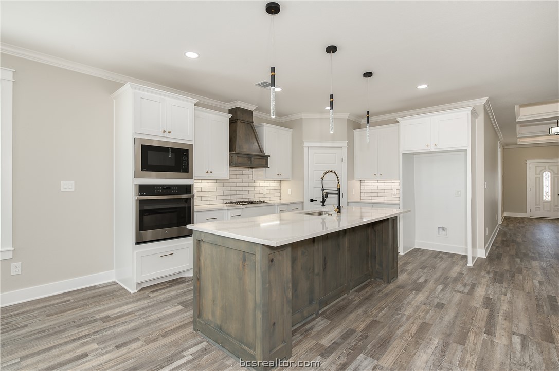 2908 GOLDBERG Drive Bryan, TX 77808 - Photo 17 of 44 Modern kitchen features: stainless steel appliances, quartz countertops, stained island, painted cabinets, decorative pendant lights, cabinet hardware, vinyl flooring, and tile backsplash.
