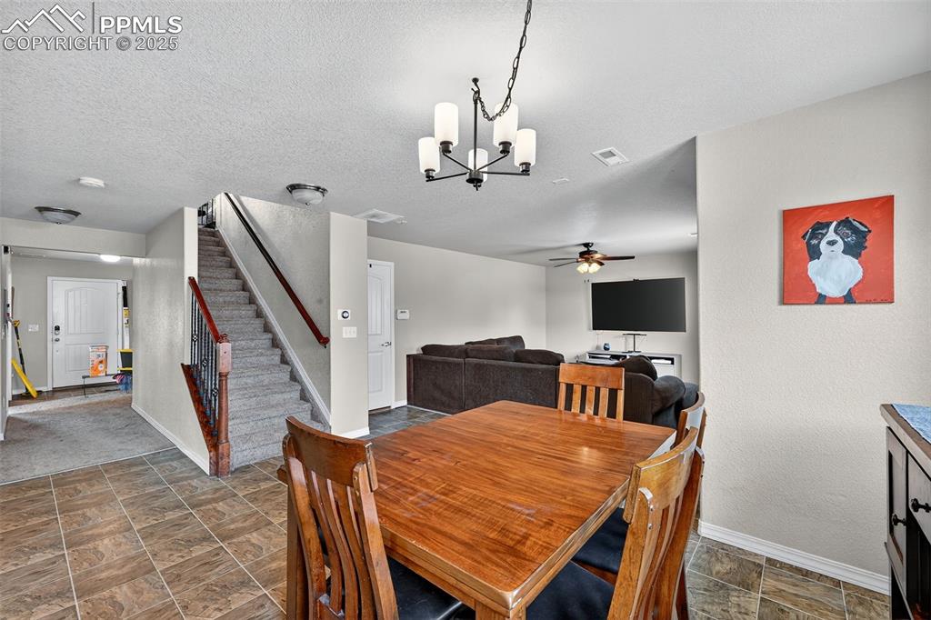 10859 Hidden Ridge Circle Peyton, CO 80831 - Photo 12 of 33 Dining space featuring stone finish floors, stairway, a chandelier, ceiling fan, and a textured ceiling
