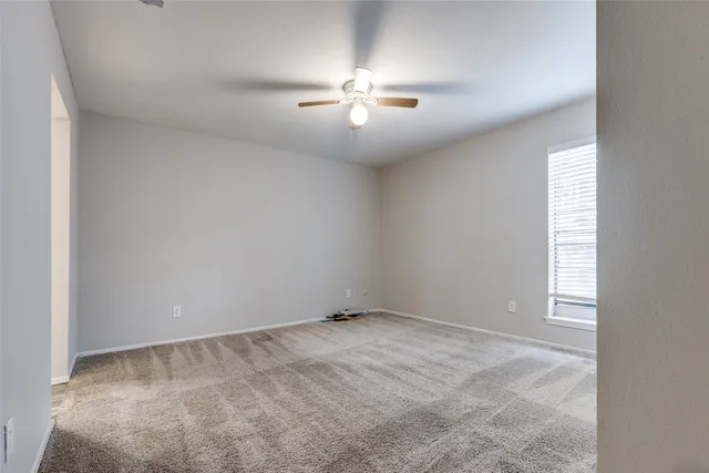 an empty room with chandelier fan and windows