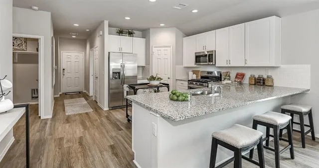 a kitchen with stainless steel appliances granite countertop a stove top oven a sink a refrigerator and white cabinets with wooden floor