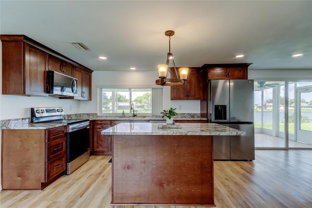 3625 Delta Place Holiday, FL 34691 - Photo 7 of 48 a large kitchen with stainless steel appliances granite countertop a stove a sink dishwasher a microwave oven and a refrigerator with wooden floor