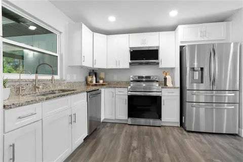 a kitchen with granite countertop a refrigerator oven a sink and white cabinets