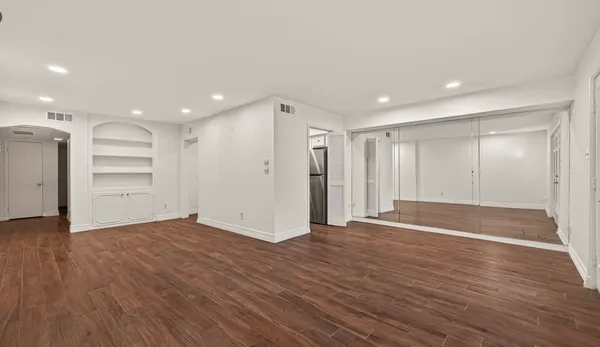 a view of an empty room with wooden floor closet and windows
