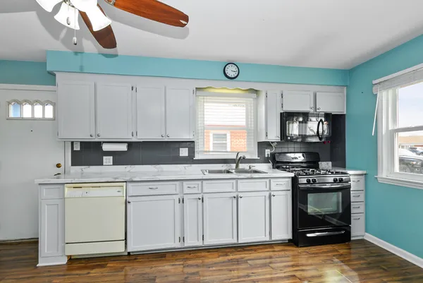a kitchen with a stove a sink and white cabinets with wooden floor