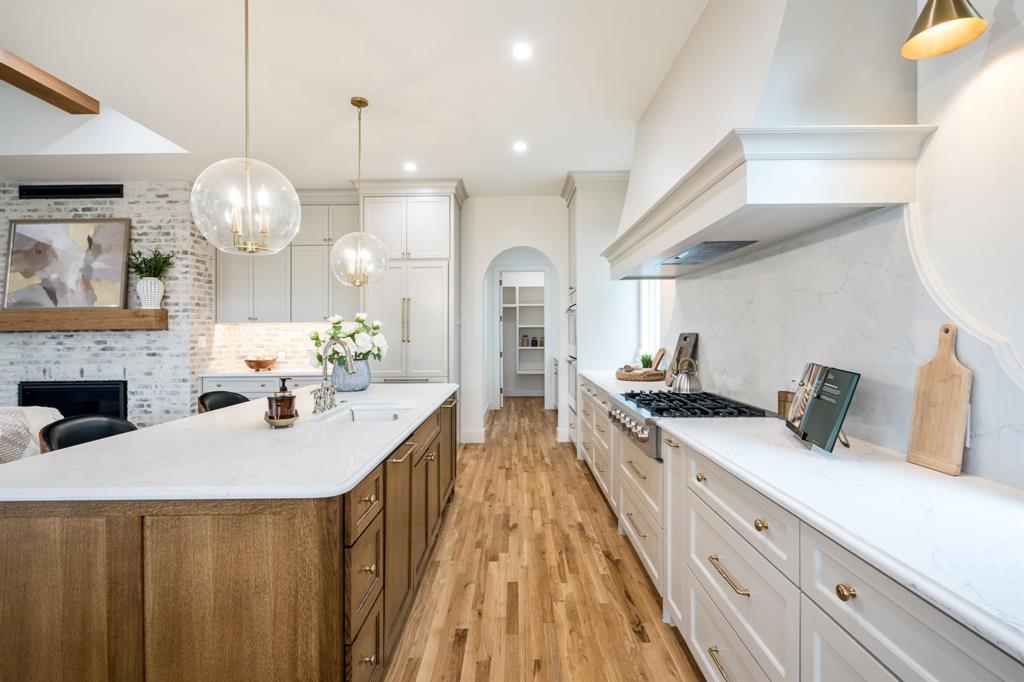 3304 Ferguson Road Grapevine, TX 76092 - Photo 16 of 38 Spacious kitchen featuring a large wood-finish island with a white countertop, two clear glass globe pendant lights, white cabinetry with gold-finish hardware, stainless steel range, and wood-finish flooring