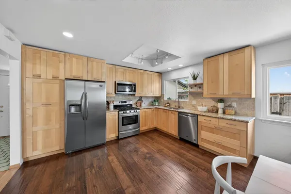 a kitchen with granite countertop a refrigerator oven a sink dishwasher and white cabinets with wooden floor