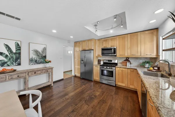 a kitchen with stainless steel appliances a stove a sink a refrigerator white cabinets and wooden floor