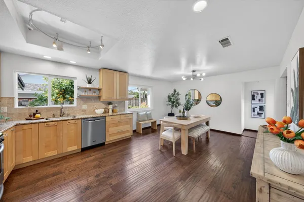 a kitchen with granite countertop a stove a sink dishwasher a dining table and chairs with wooden floor