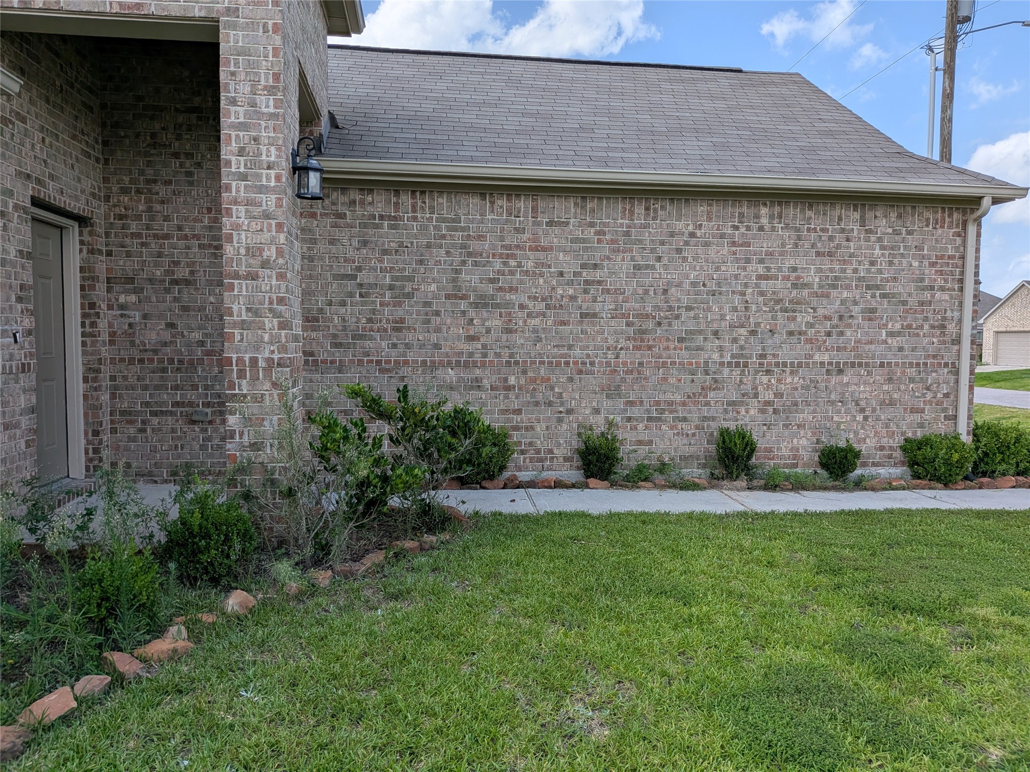 15730 Joe Dimaggio Street Splendora, TX 77372 - Photo 3 of 20 This photo shows the side of a brick house with a well-maintained lawn and some small shrubs along the walkway. The exterior features a classic brick finish and a sloped roof.