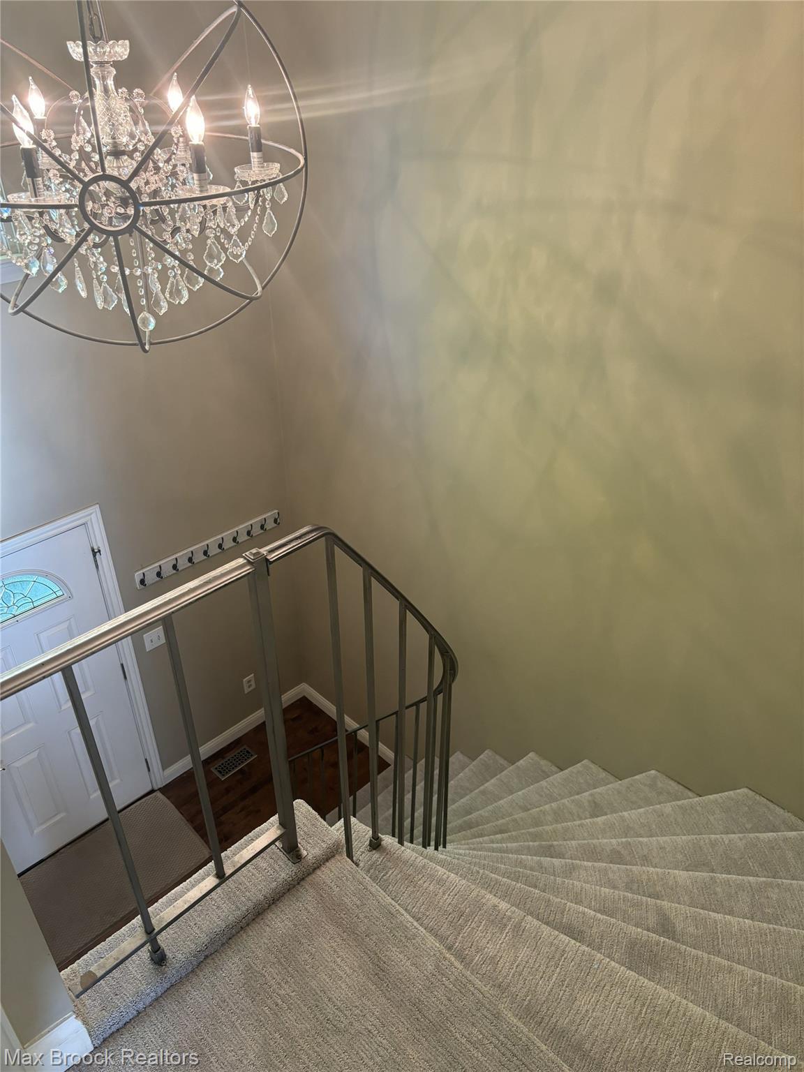 Spiral staircase with light-toned carpet, metallic railing, and an ornate crystal chandelier