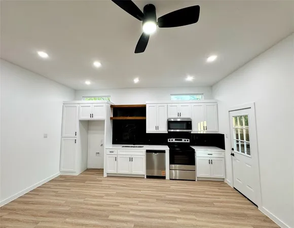 a kitchen with stainless steel appliances kitchen island granite countertop a stove top oven a sink a refrigerator and white cabinets with wooden floor