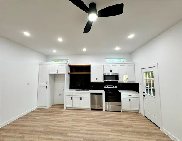 a kitchen with stainless steel appliances kitchen island granite countertop a stove top oven a sink a refrigerator and white cabinets with wooden floor