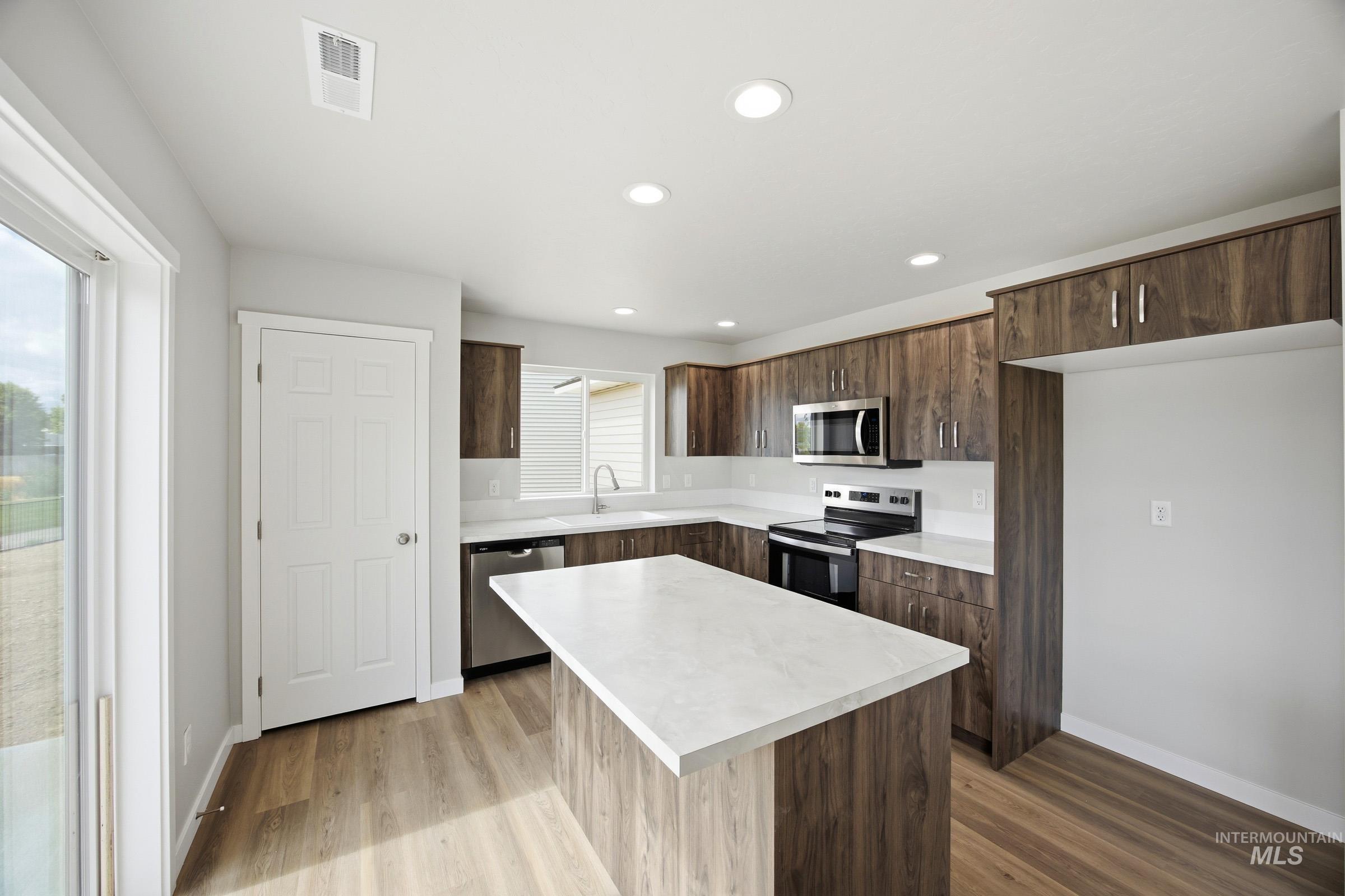 14044 Shiny Spruce Street Caldwell, ID 83607 - Photo 3 of 24 Modern kitchen featuring wood-finish cabinetry, light-toned countertops, stainless steel appliances, and a central island