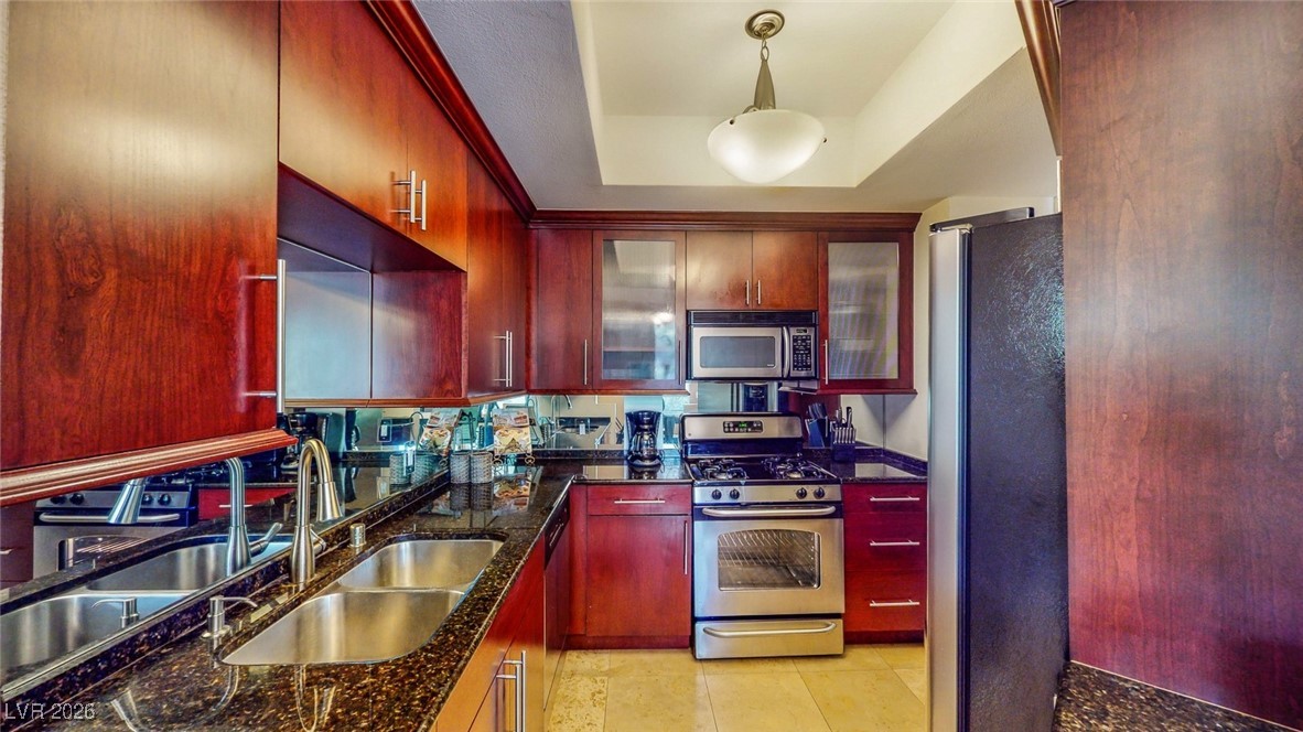 260 East Flamingo Road, Unit 229 Las Vegas, NV 89169 - Photo 26 of 31 Kitchen featuring stainless steel appliances, bold wood finish cabinetry, decorative light fixtures, dark stone countertops, and a tray ceiling