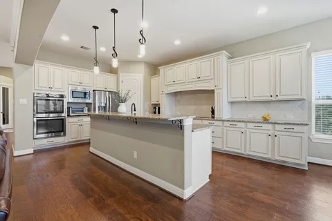 a kitchen with granite countertop lots of white cabinets and wooden floor