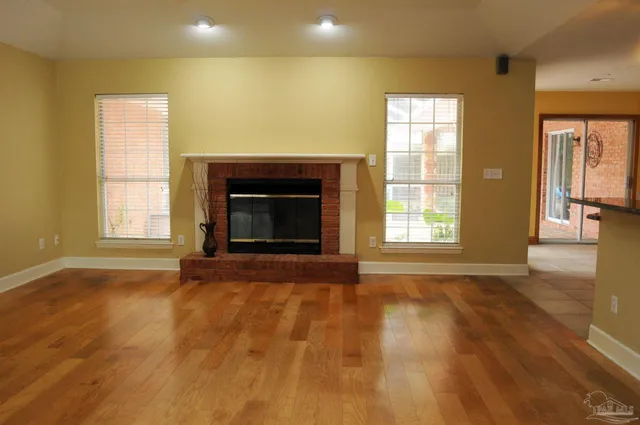 an empty room with wooden floor fireplace and windows
