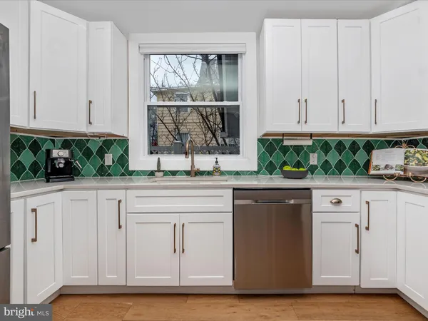 a kitchen with stainless steel appliances granite countertop a coffee maker a sink and white cabinets with wooden floor