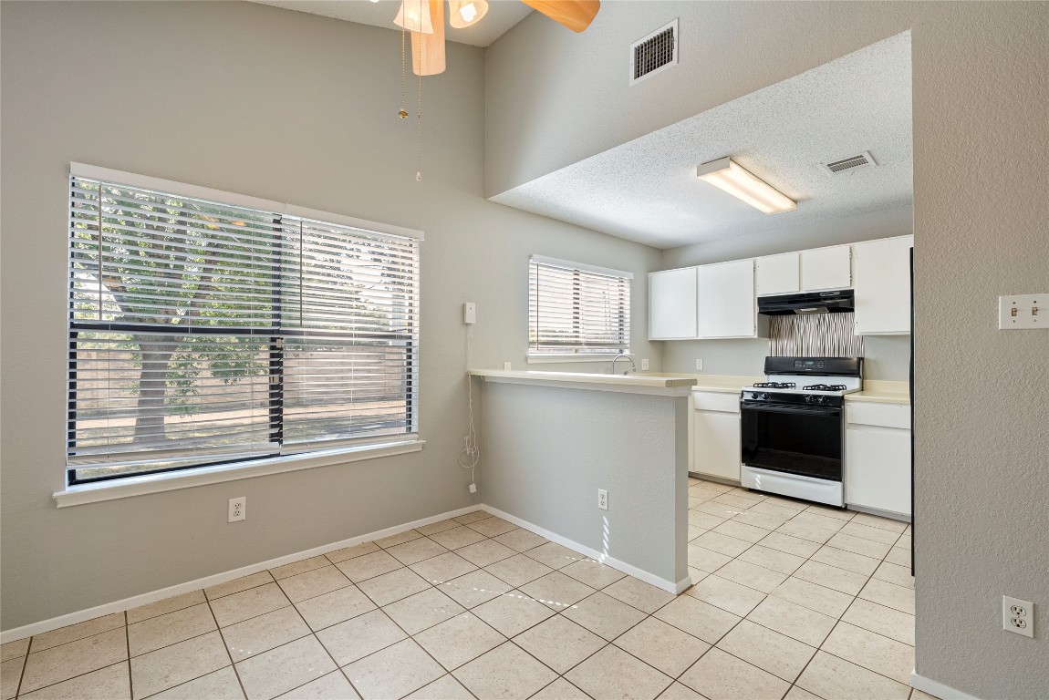 14433 Robert I Walker Boulevard Austin, TX 78728 - Photo 6 of 15 Kitchen featuring light countertops, light tile patterned floors, white cabinets, range with gas stovetop, and a textured ceiling
