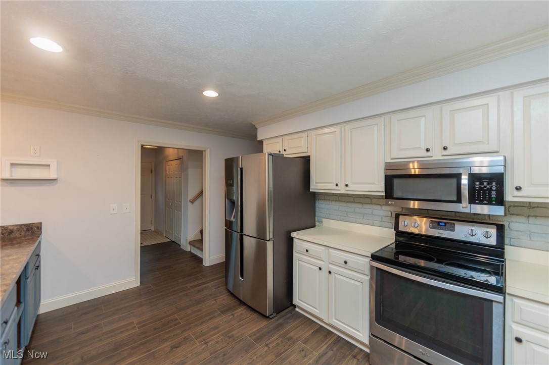 28013 Knickerbocker Road Bay Village, OH 44140 - Photo 13 of 38 Kitchen featuring stainless steel appliances, dark wood-style floors, light countertops, tasteful backsplash, and crown molding