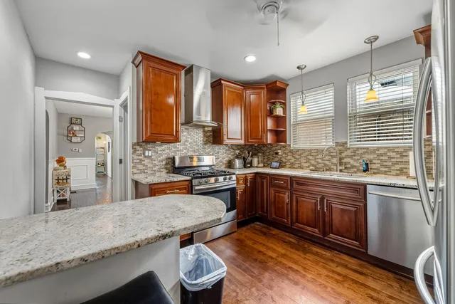 a kitchen with stainless steel appliances granite countertop wooden cabinets a sink a stove a dining table and chairs