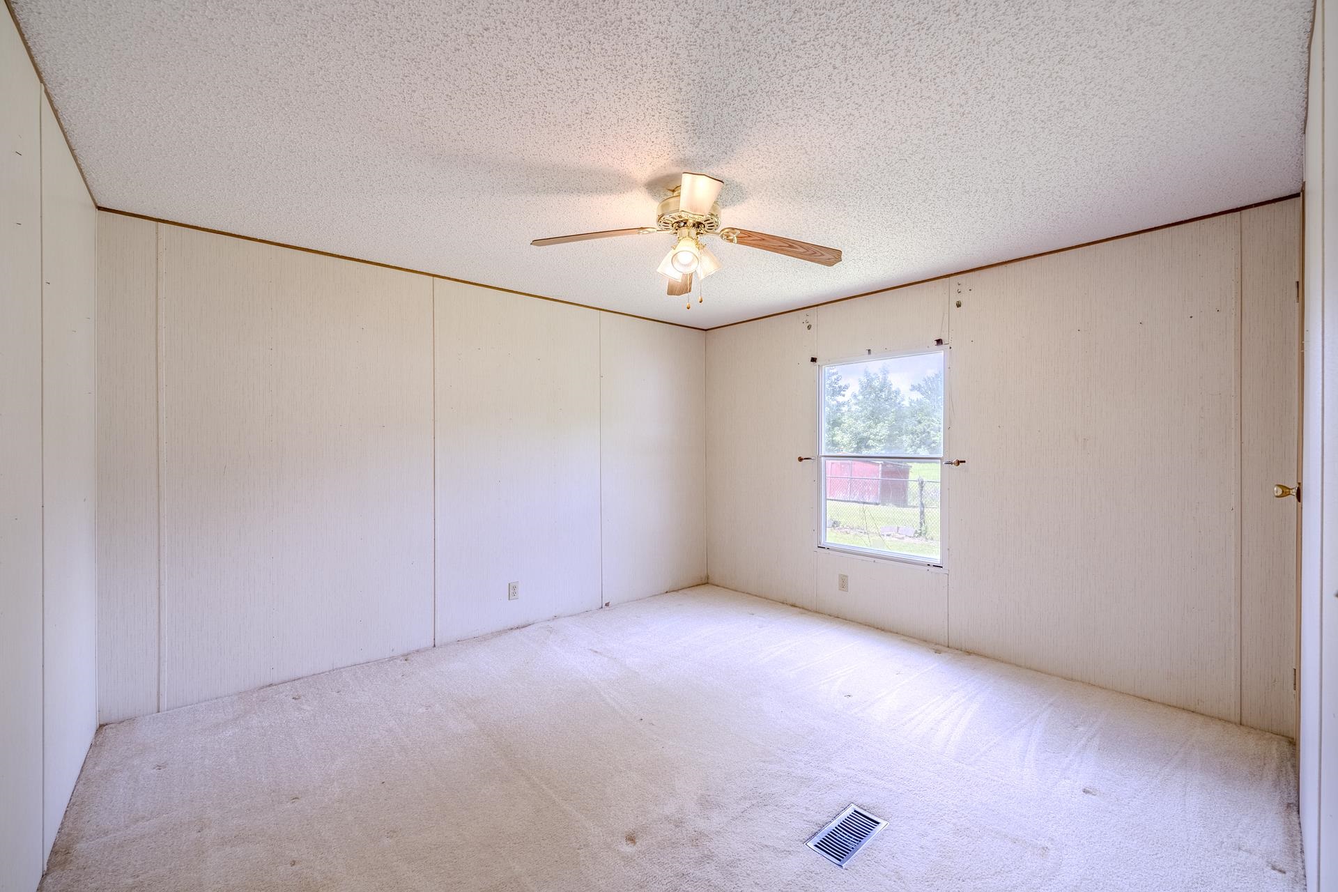 859 Old Morris Chapel Road Adamsville, TN 38310 - Photo 32 of 39 Room featuring a textured ceiling, a ceiling fan with light fixture, light-colored walls with vertical paneling, and a window with an exterior view