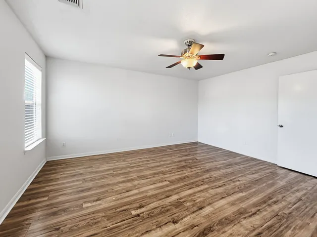 a view of empty room with wooden floor and fan