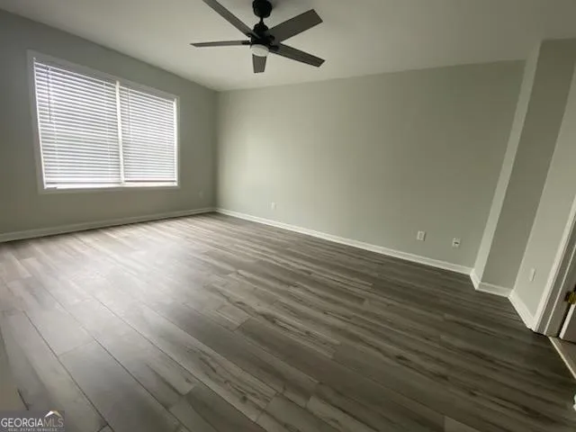 an empty room with wooden floor fan and windows