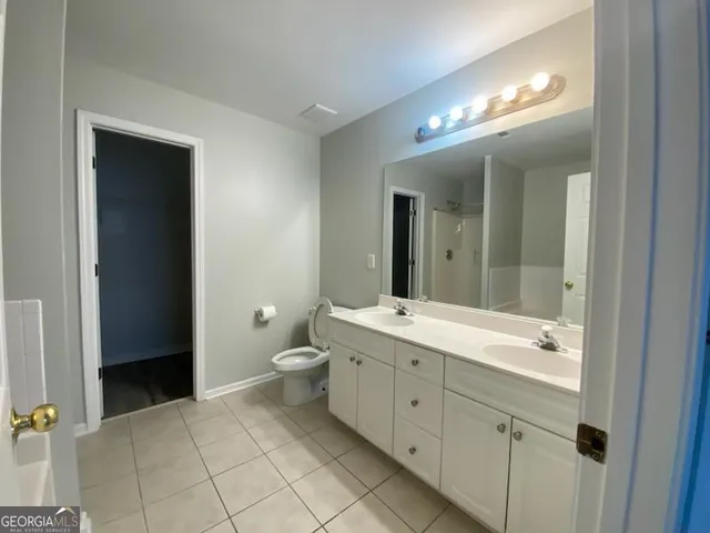 a spacious bathroom with a double vanity sink a toilet and a mirror