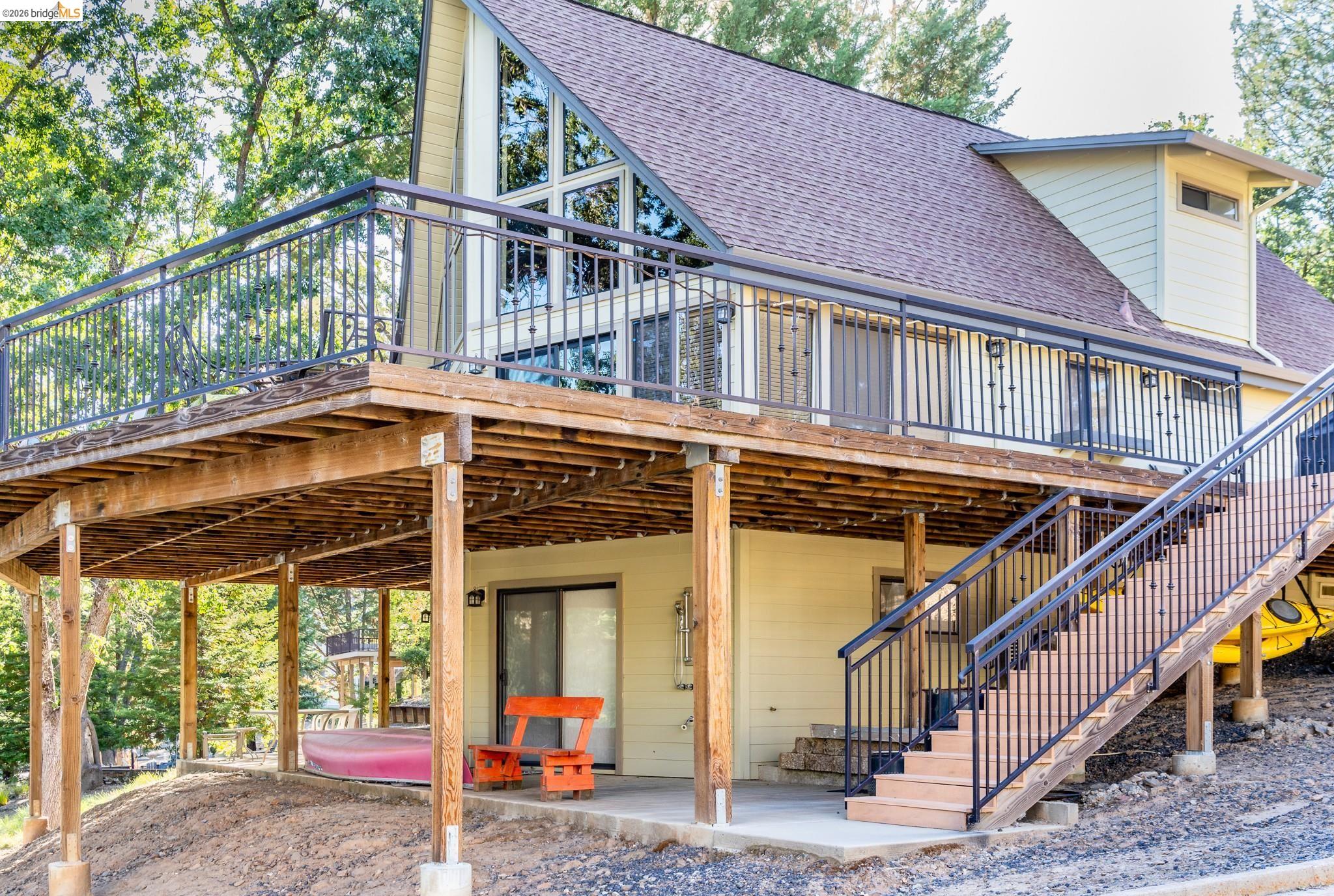 19711 Pleasantview Drive Groveland, CA 95321 - Photo 12 of 39 Contemporary A-frame residence featuring a spacious upper-level deck with black iron railings, a lower-level concrete patio, a prominent exterior staircase with matching railings, a sliding glass door entry, and a dormer window
