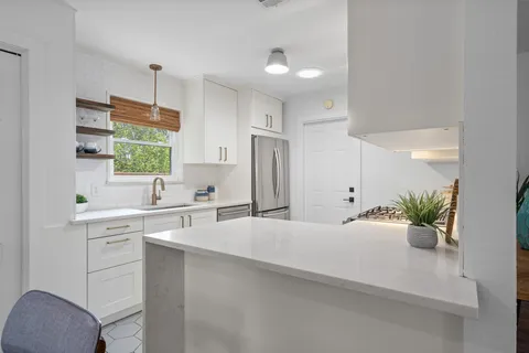 a view of a kitchen with kitchen island a window a sink and cabinets