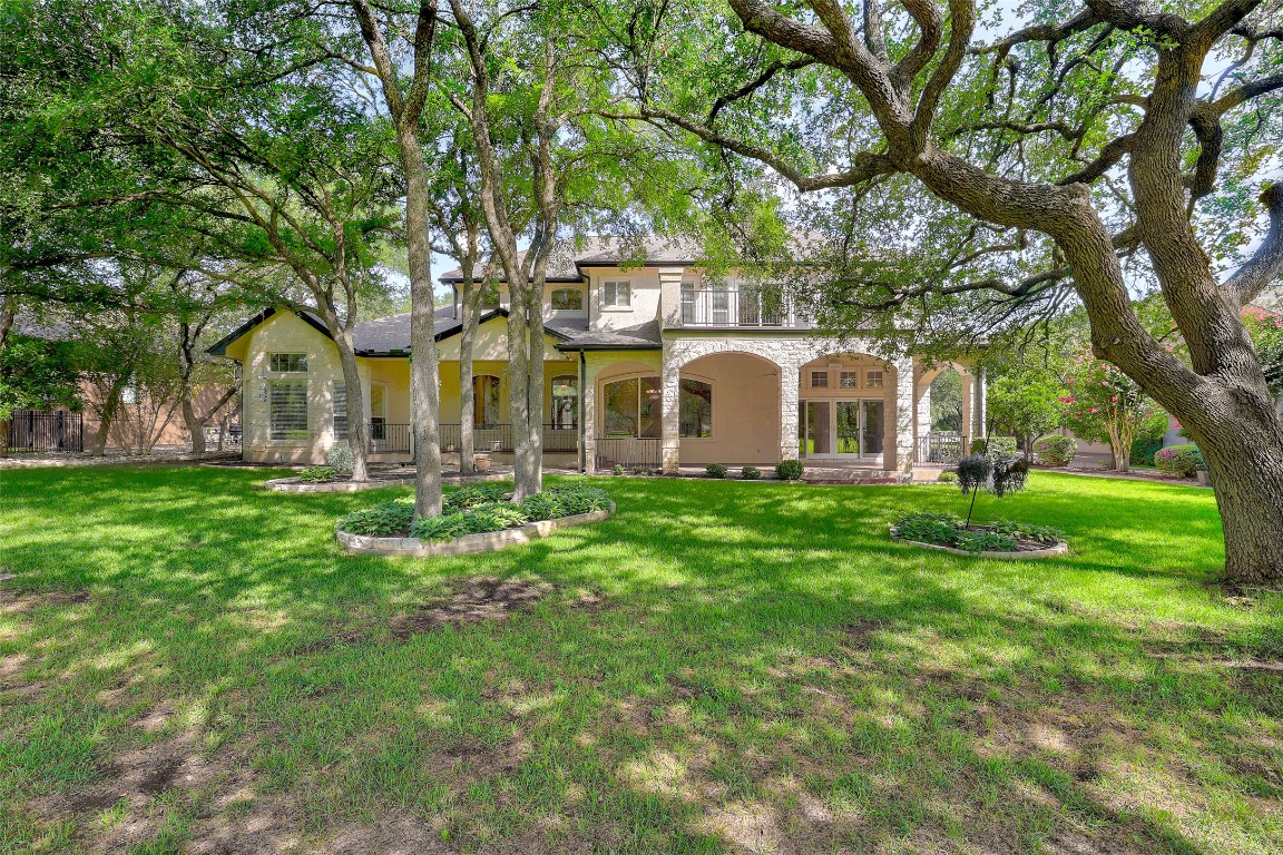 a view of a white house with a big yard plants and large trees