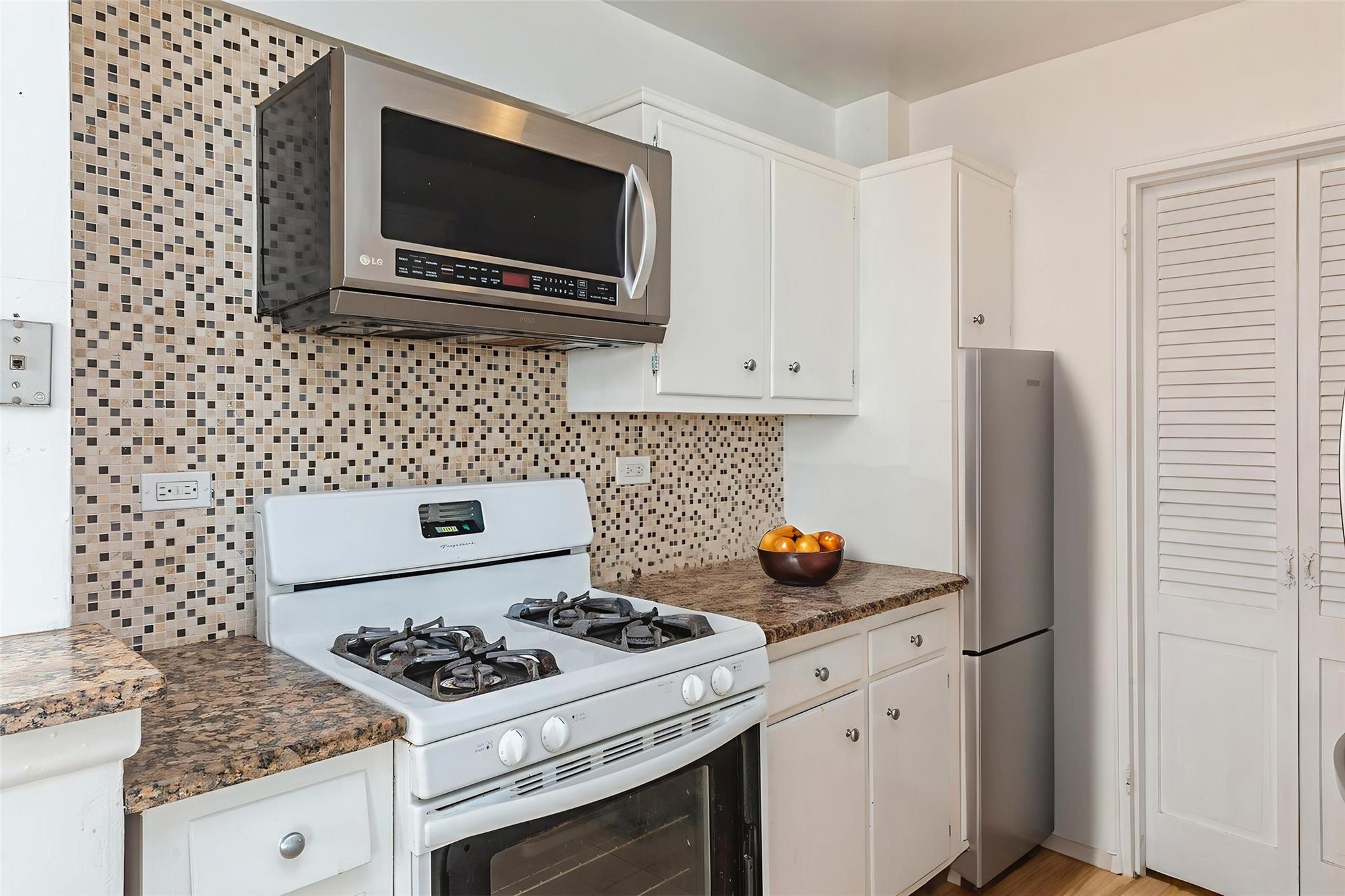 99-10 60th Avenue, Unit 1C1 Queens, NY 11368 - Photo 4 of 8 Kitchen with stainless steel appliances, decorative backsplash, white cabinets, and dark countertops
