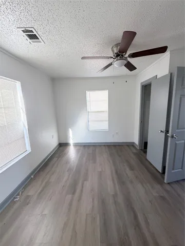 an empty room with wooden floor fan and windows
