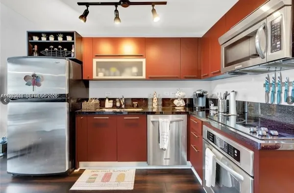 a kitchen with stainless steel appliances granite countertop a refrigerator a stove and a sink with wooden floors