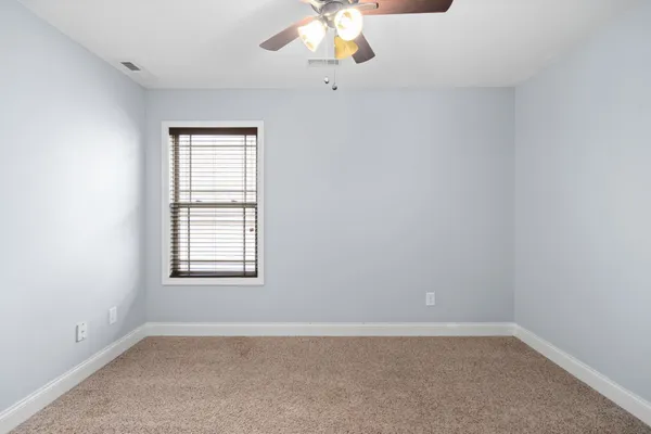 an empty room with a chandelier fan and windows