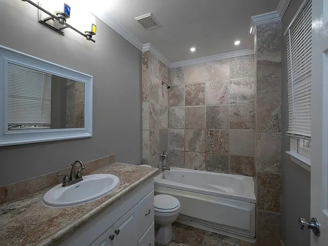 a bathroom with a granite countertop sink toilet mirror and bathtub