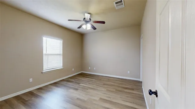 an empty room with wooden floor fan and windows