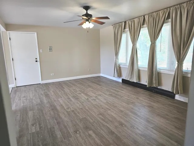 an empty room with wooden floor fan and windows