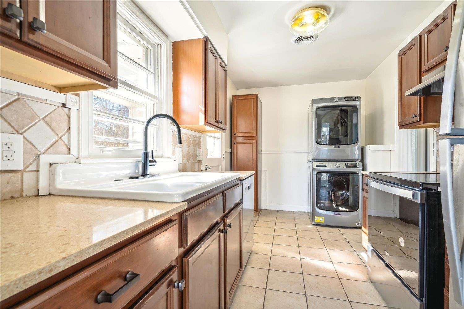3901 Lytle Circle Memphis, TN 38122 - Photo 11 of 30 Kitchen featuring light tile patterned flooring, brown cabinets, stacked washing maching and dryer, and light stone counters