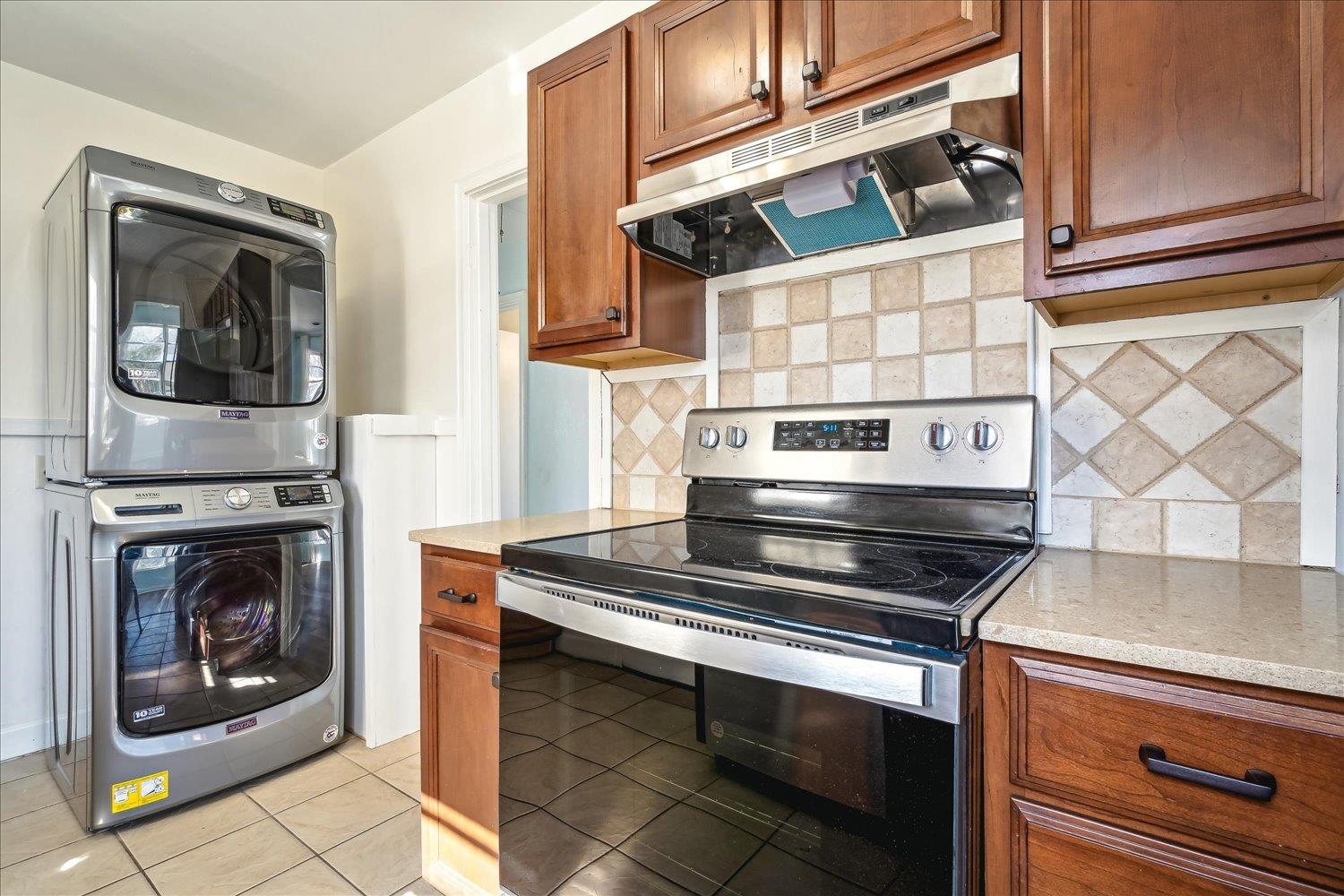 3901 Lytle Circle Memphis, TN 38122 - Photo 14 of 30 Kitchen featuring light tile patterned floors, stainless steel electric range, stacked washer and clothes dryer, under cabinet range hood, and brown cabinets