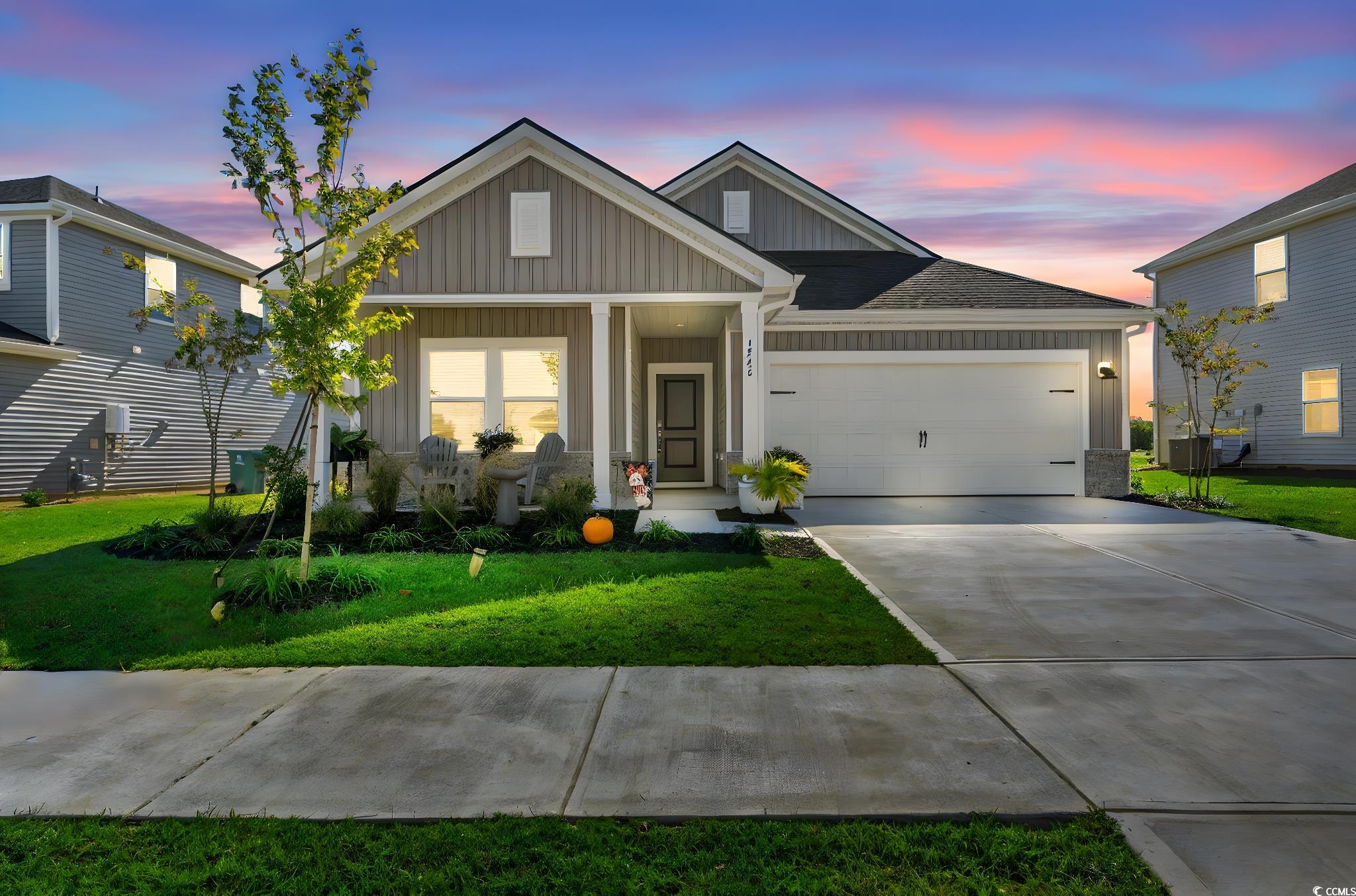 View of front of property featuring board and batten siding, a lawn, concrete driveway, and a porch