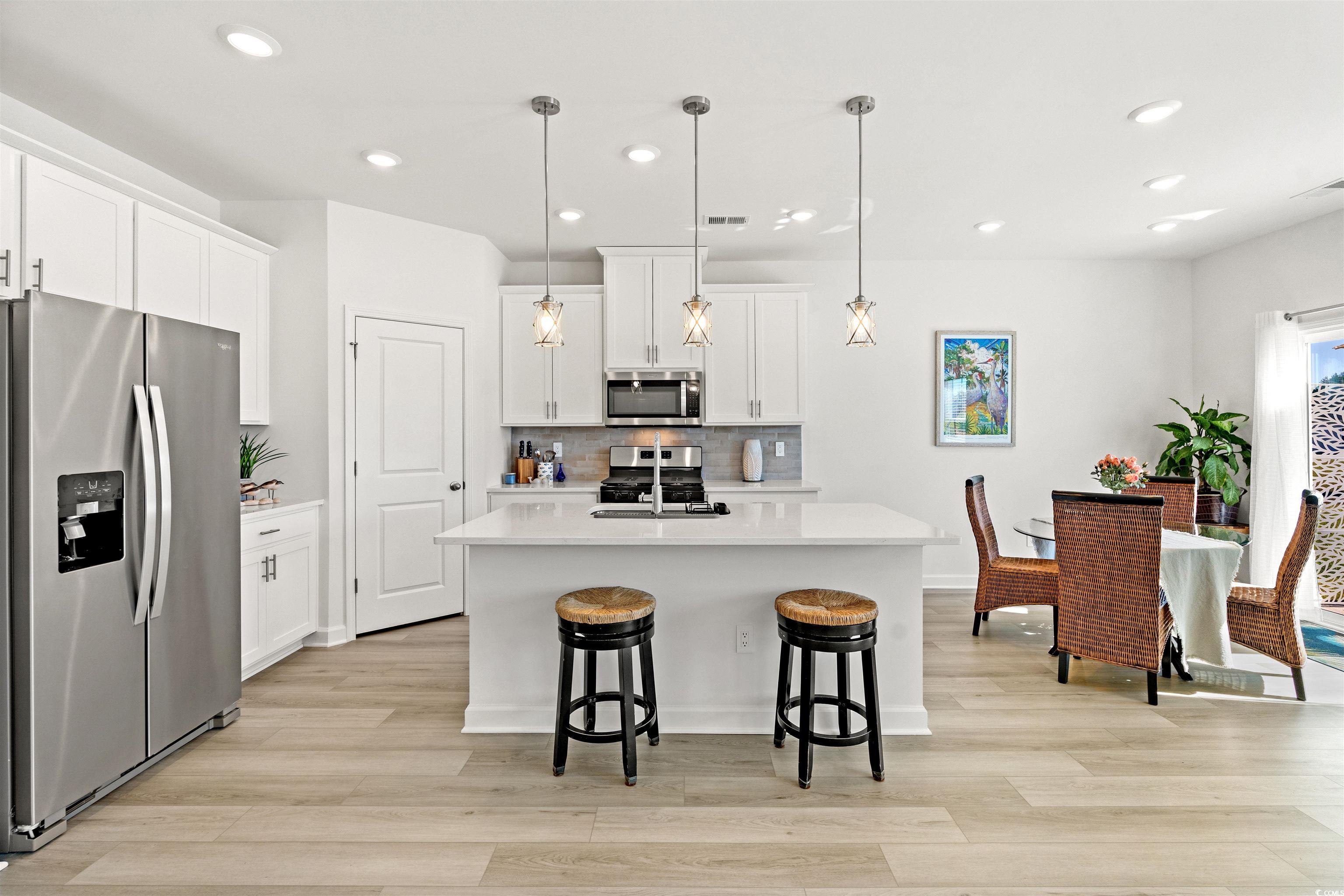 1546 Regal Fern Way Longs, SC 29568 - Photo 5 of 34 Kitchen featuring appliances with stainless steel finishes, decorative backsplash, white cabinets, hanging light fixtures, and light wood-type flooring