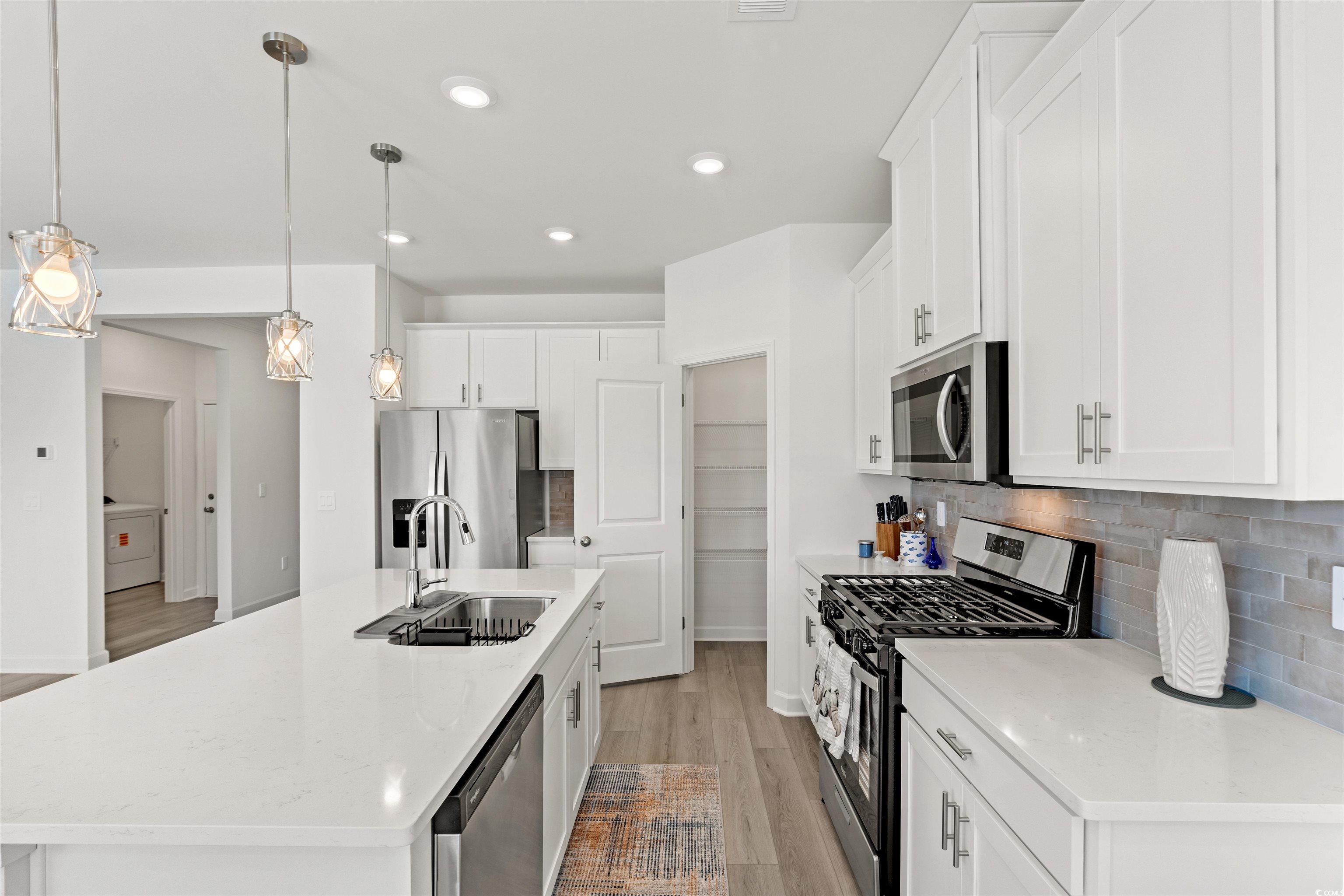 1546 Regal Fern Way Longs, SC 29568 - Photo 6 of 34 Kitchen featuring appliances with stainless steel finishes, tasteful backsplash, hanging light fixtures, light wood-type flooring, and a center island with sink